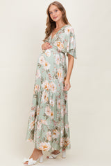 woman wearing a floral mint green maternity maxi dress with short sleeves and a v-neck, cradling her baby bump