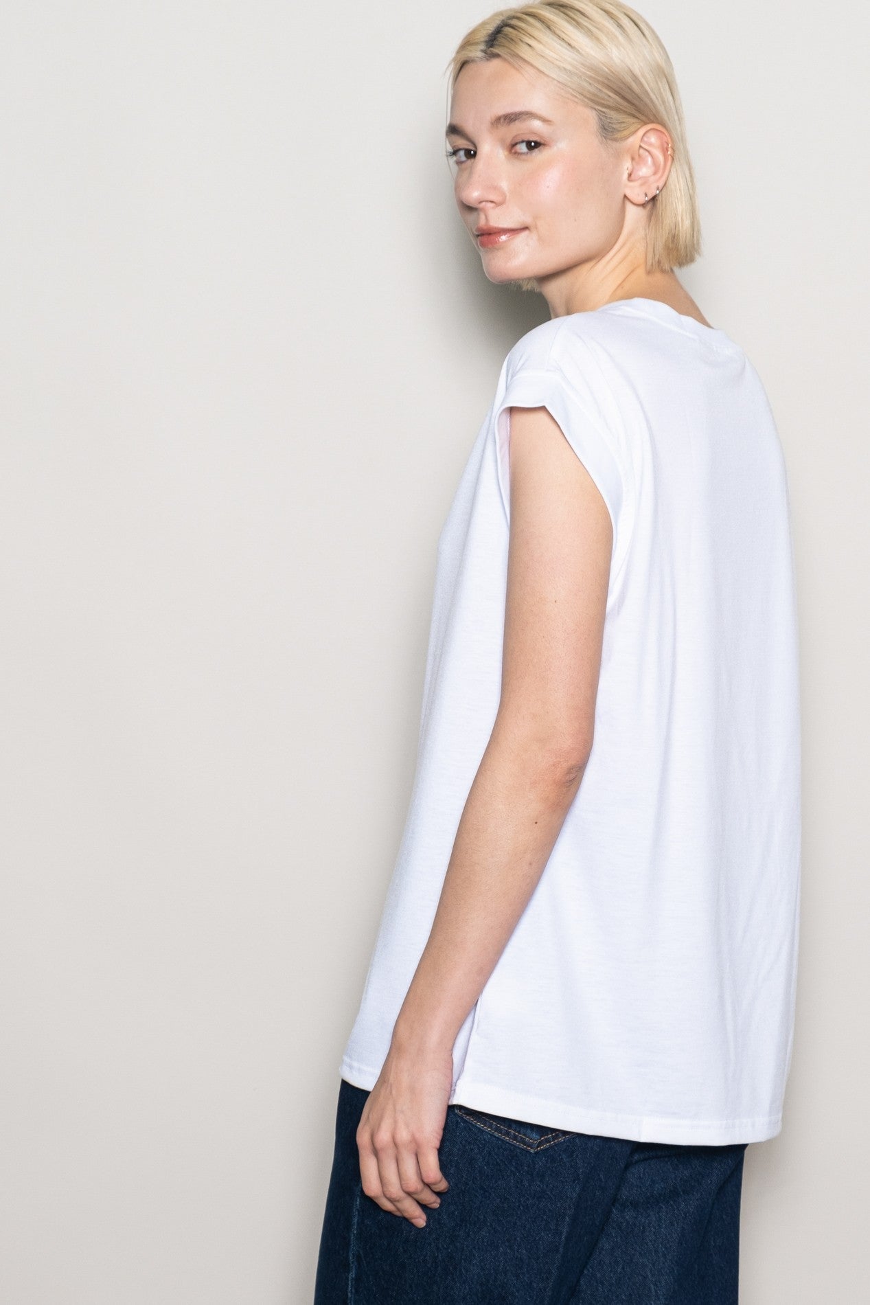 woman wearing a white casual t-shirt with rolled sleeves, featuring a relaxed fit and styled with dark blue jeans