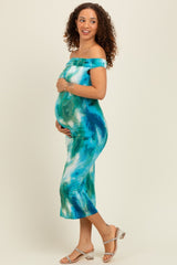 woman wearing a teal and blue tie-dye off-shoulder maternity dress and holding her baby bump