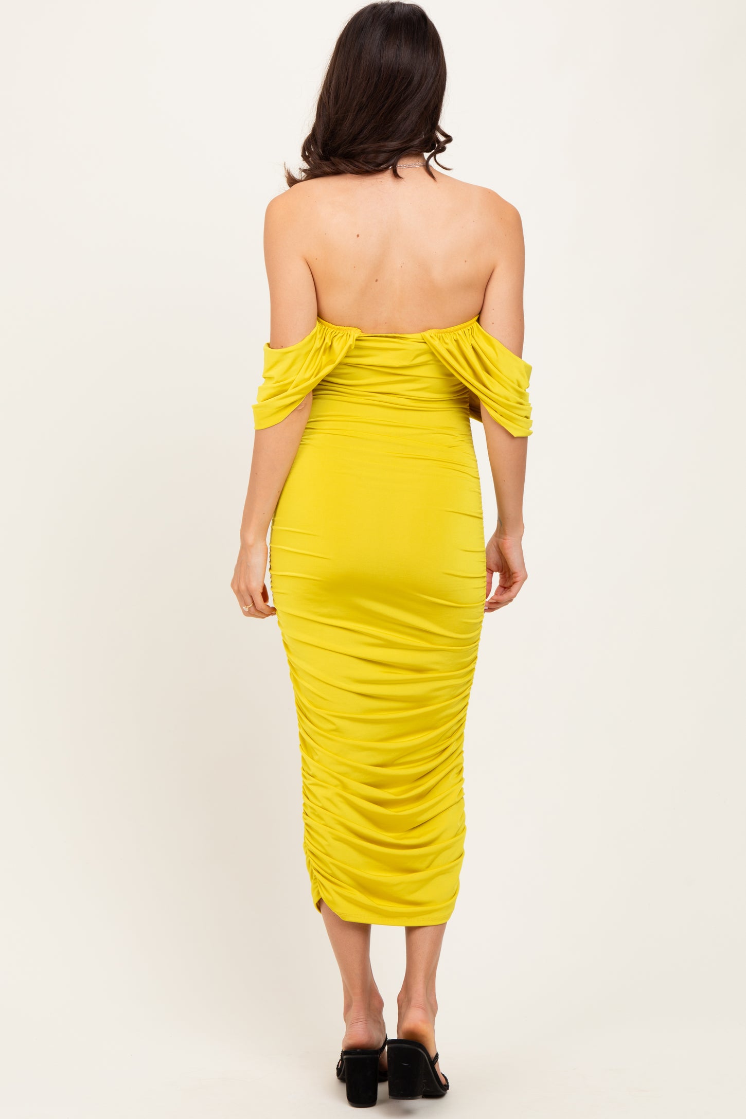 woman wearing a bright yellow off-the-shoulder bodycon dress with ruched detailing, viewed from the back