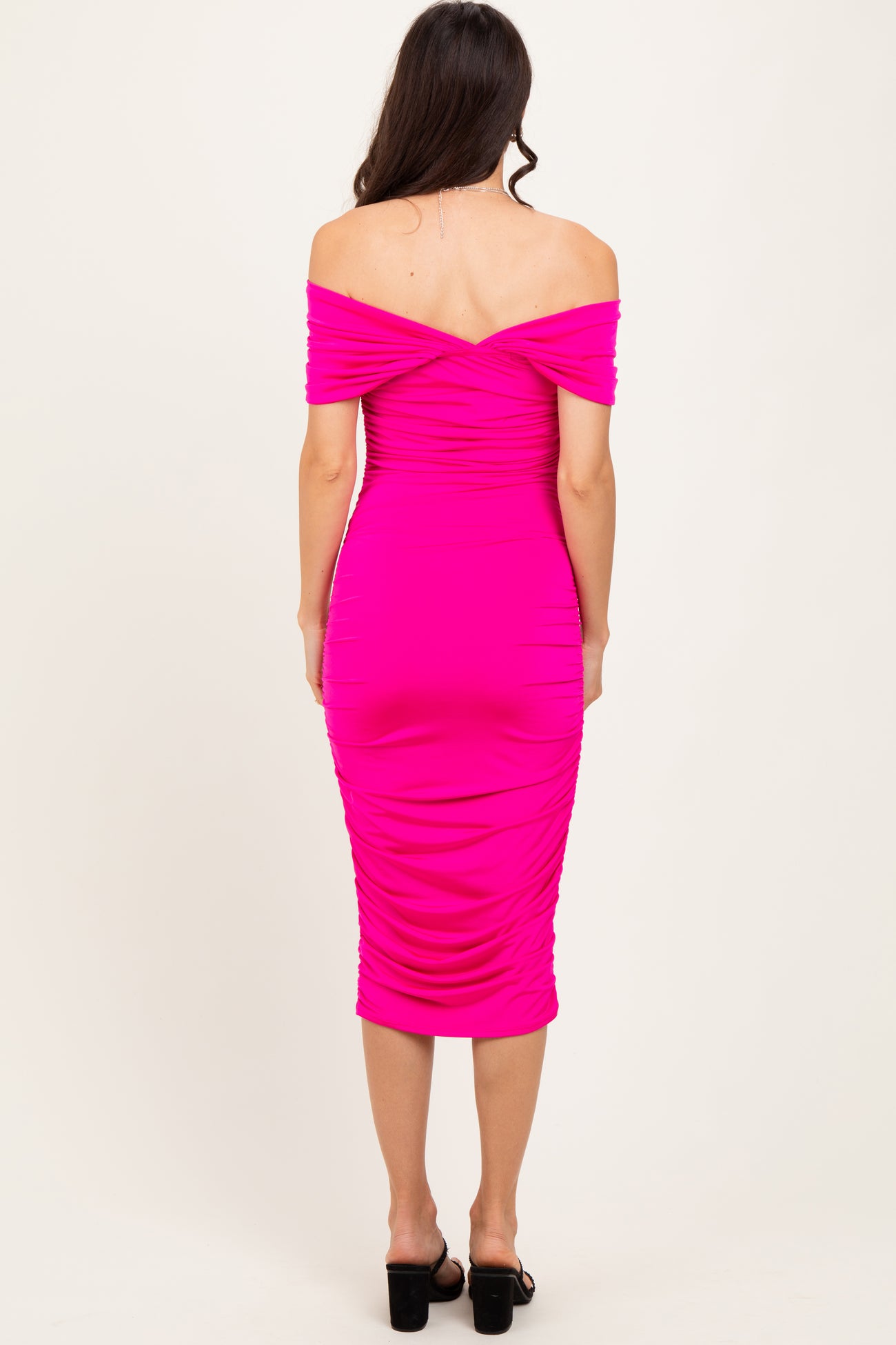 woman wearing a pink off-the-shoulder bodycon dress with ruching detail and a fitted midi length, shown from the back