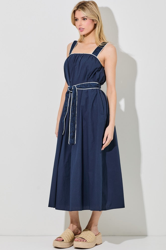 woman wearing a navy blue sleeveless midi dress with a cinched waist and a matching belt, styled with beige platform sandals
