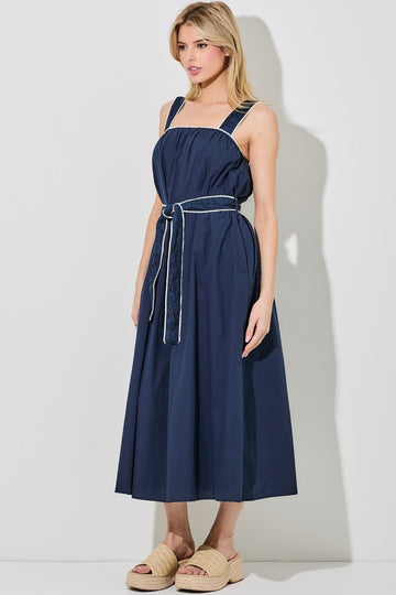 woman wearing a navy blue sleeveless midi dress with a cinched waist and a matching belt, styled with beige platform sandals
