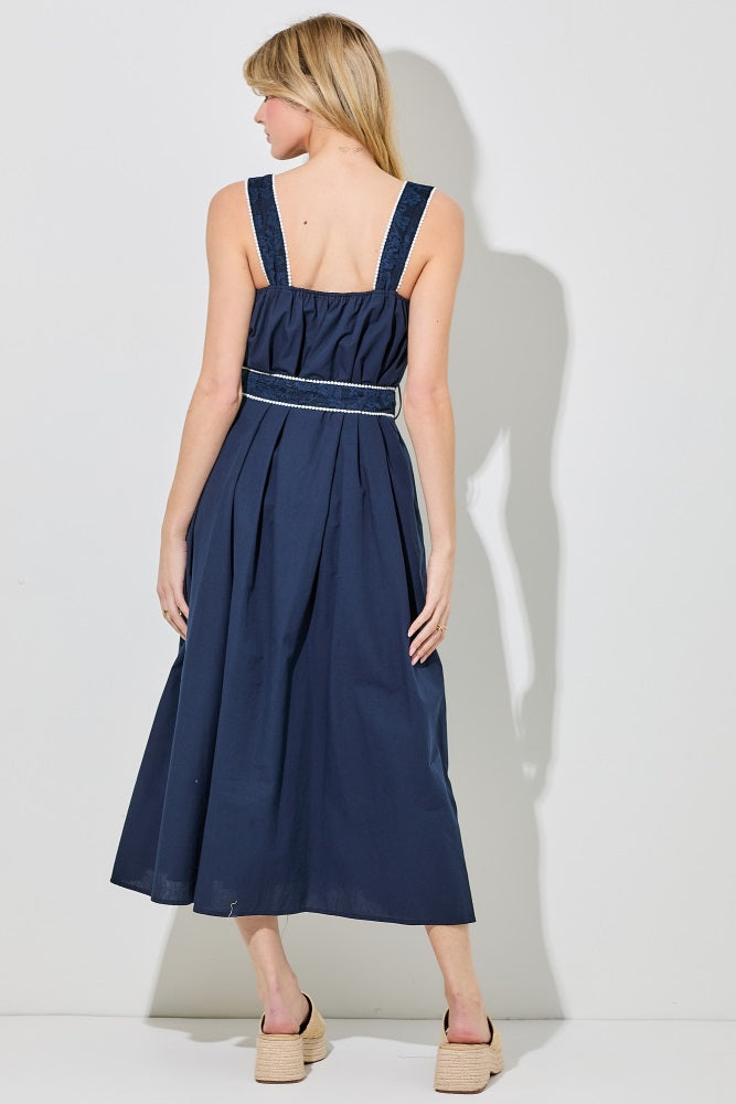 woman wearing a navy blue maxi dress with adjustable straps and a gathered waist, standing with her back to the camera