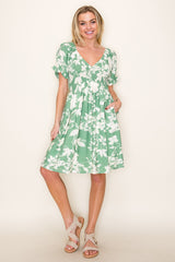 woman wearing a green floral print knee-length dress with short sleeves and pockets