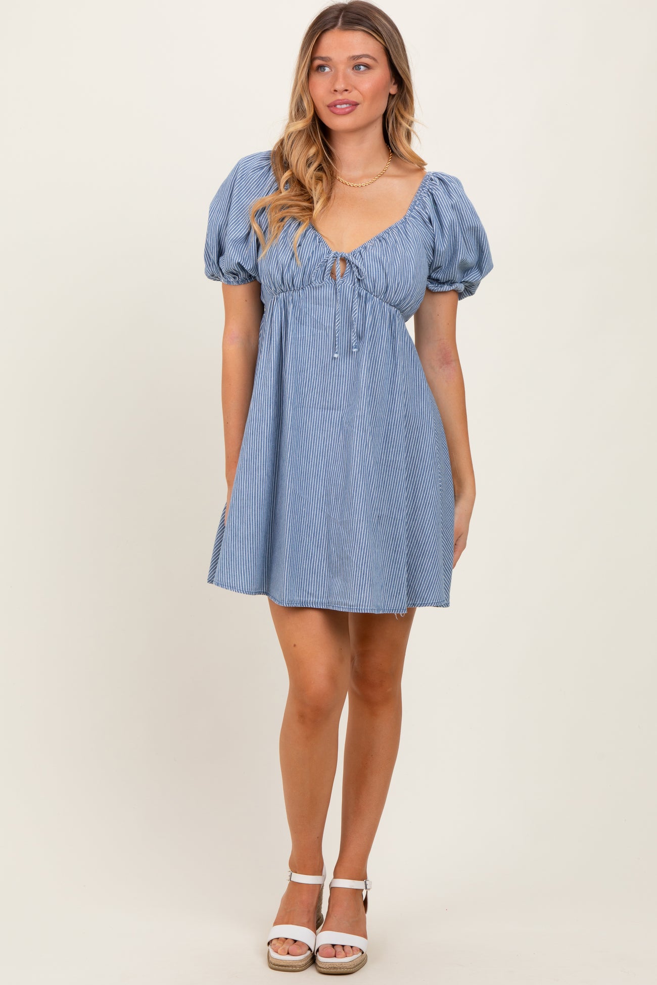 woman wearing a light blue striped puff sleeve dress with a tie front detail and a flared skirt