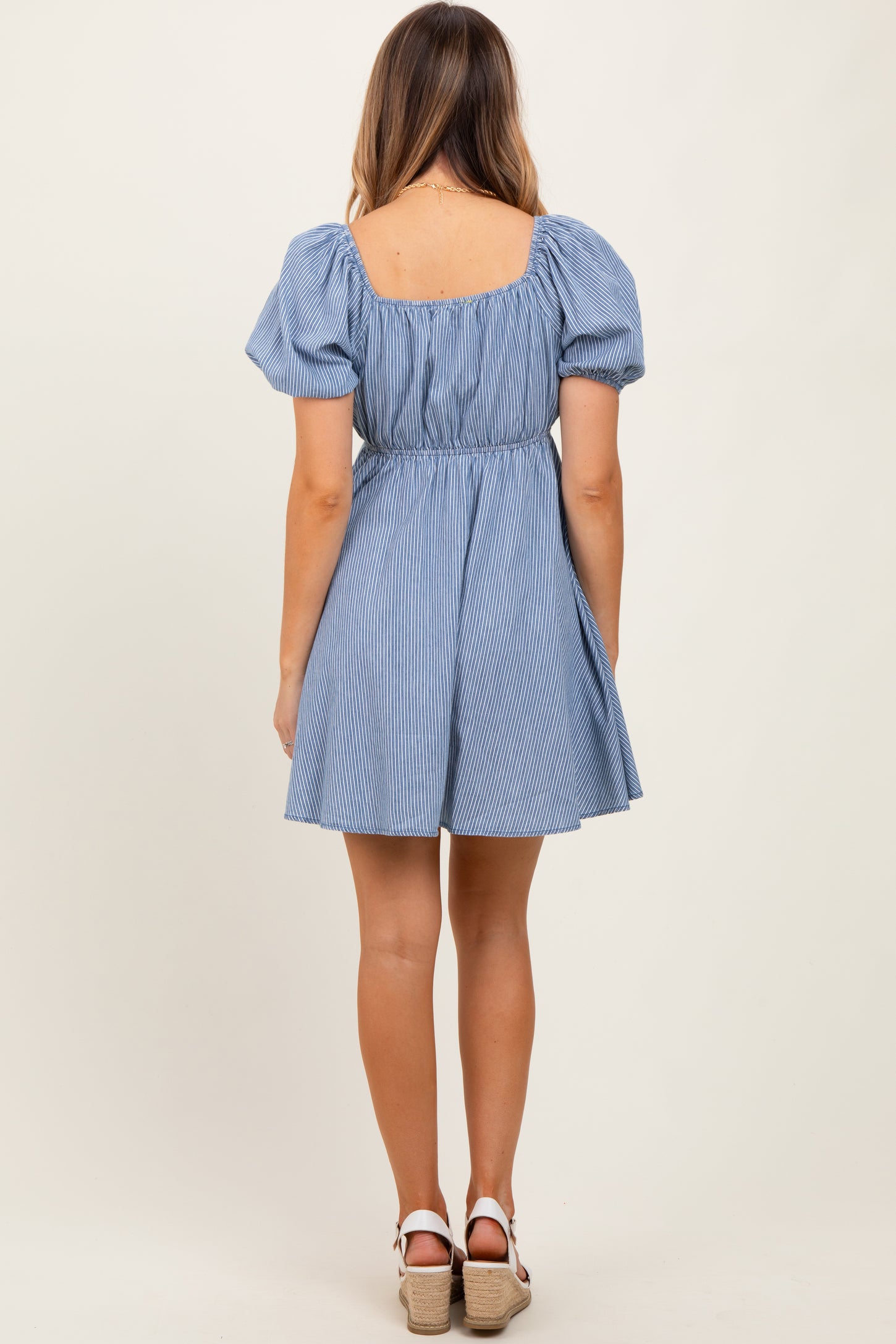 woman wearing a blue and white striped short dress with puff sleeves and a fitted waist, view from the back