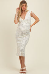 woman wearing a white floral print maternity dress with a deep V-neck and tie sleeves, showing her baby bump