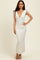 woman wearing a white floral maxi dress with a deep v-neck and tie straps, standing on a light background