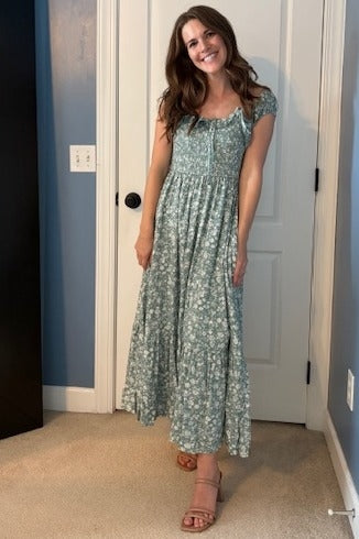 woman wearing a green floral maxi dress with short sleeves and a button front, standing in a brightly lit room