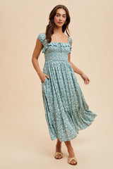 woman wearing a light blue floral maxi dress with short ruffled sleeves and pockets, standing on a neutral background
