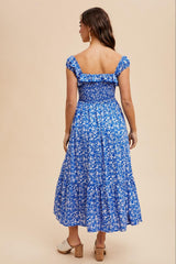 woman wearing a blue floral off-the-shoulder maxi dress with a smocked bodice and tiered skirt, showing the back view