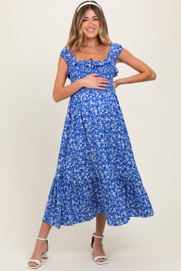 woman wearing a blue floral maternity dress with ruffle sleeves and holding her baby bump