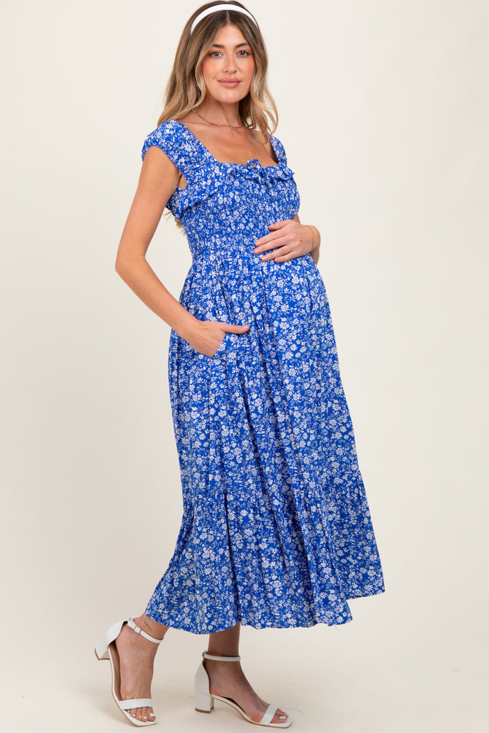 woman wearing a blue floral maternity dress with short sleeves and pockets, holding her baby bump