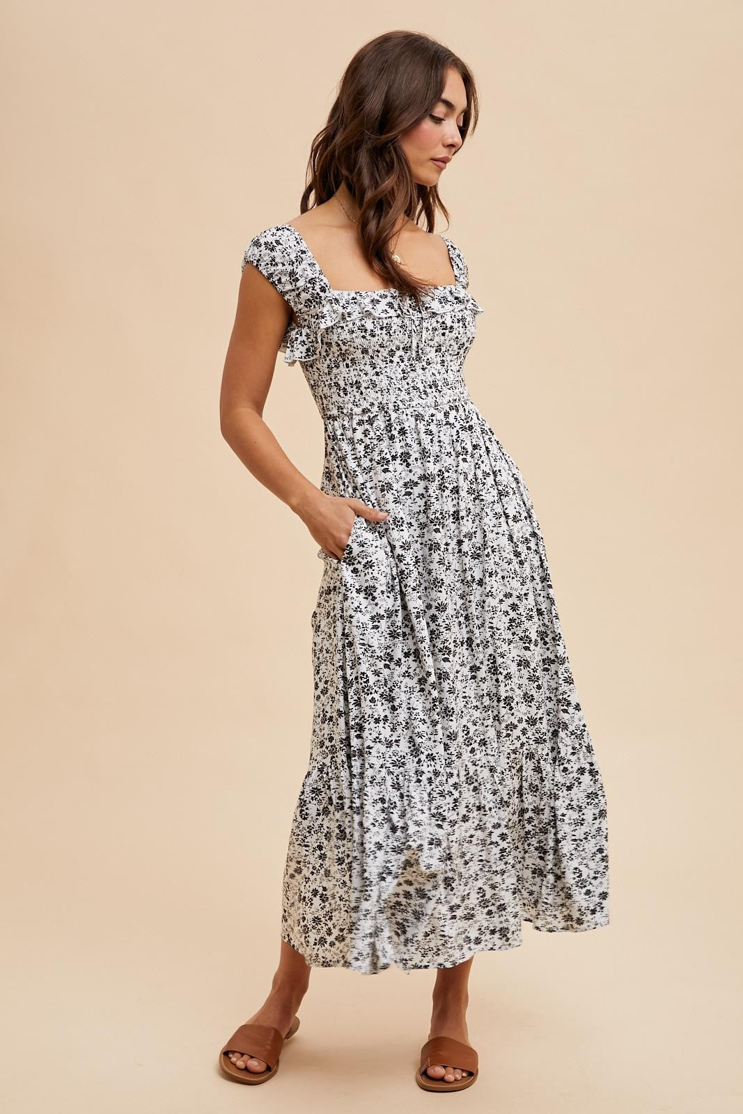 woman wearing a black and white floral maxi dress with smocked bodice and pockets, standing on a beige background