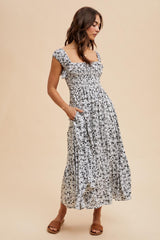 woman wearing a black and white floral maxi dress with smocked bodice and pockets, standing on a beige background