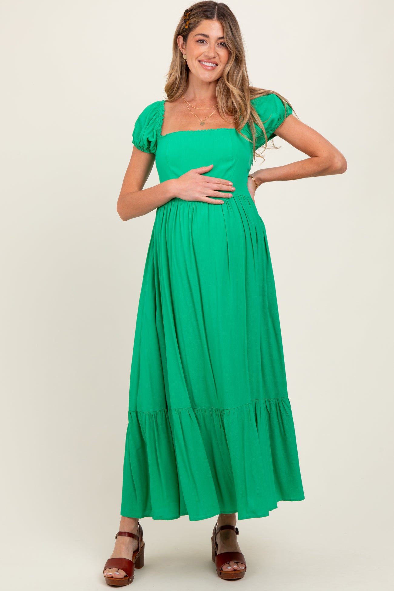 woman wearing a bright green maternity dress with puff sleeves and a flowy skirt, holding her baby bump