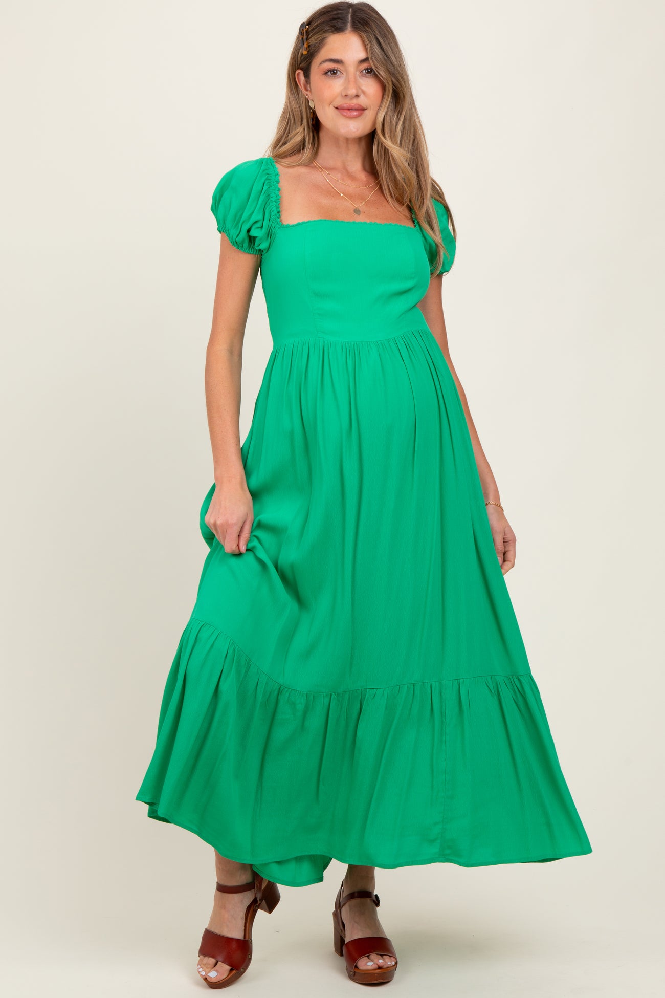 woman wearing a bright green maternity maxi dress with puff sleeves and a ruffled hem, showing her baby bump