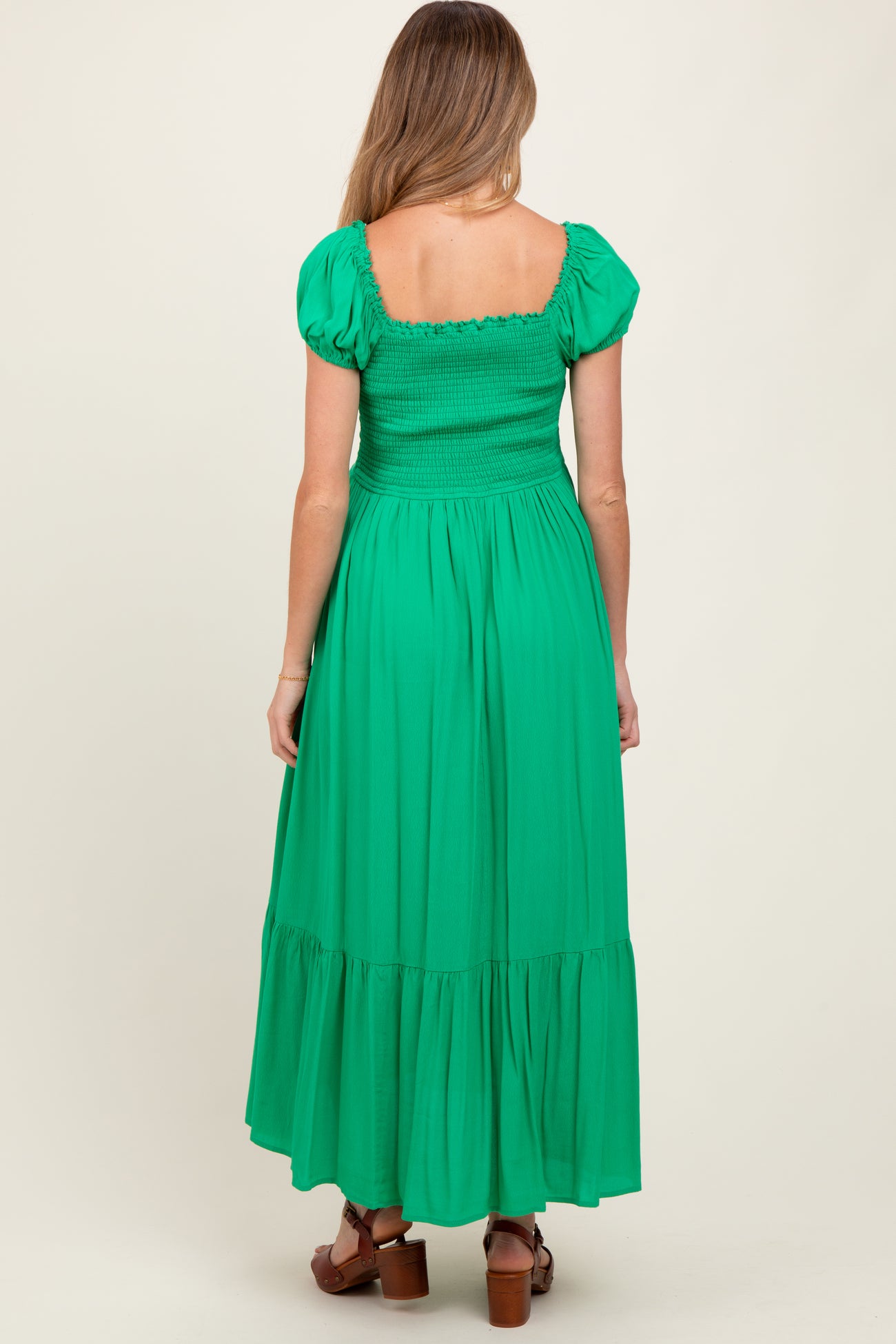 woman wearing a bright green smocked maternity maxi dress with puff sleeves and a tiered skirt, showing her back