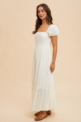 woman wearing a cream-colored maxi dress with puff sleeves and a square neckline, posing against a light background