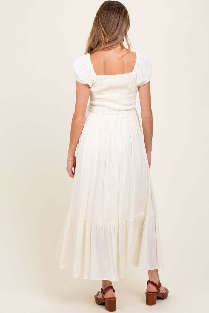 woman wearing a cream maternity maxi dress with puff sleeves and a smocked bodice, viewed from the back
