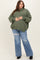woman wearing an oversized olive green sweater and distressed blue jeans, showcasing her baby bump