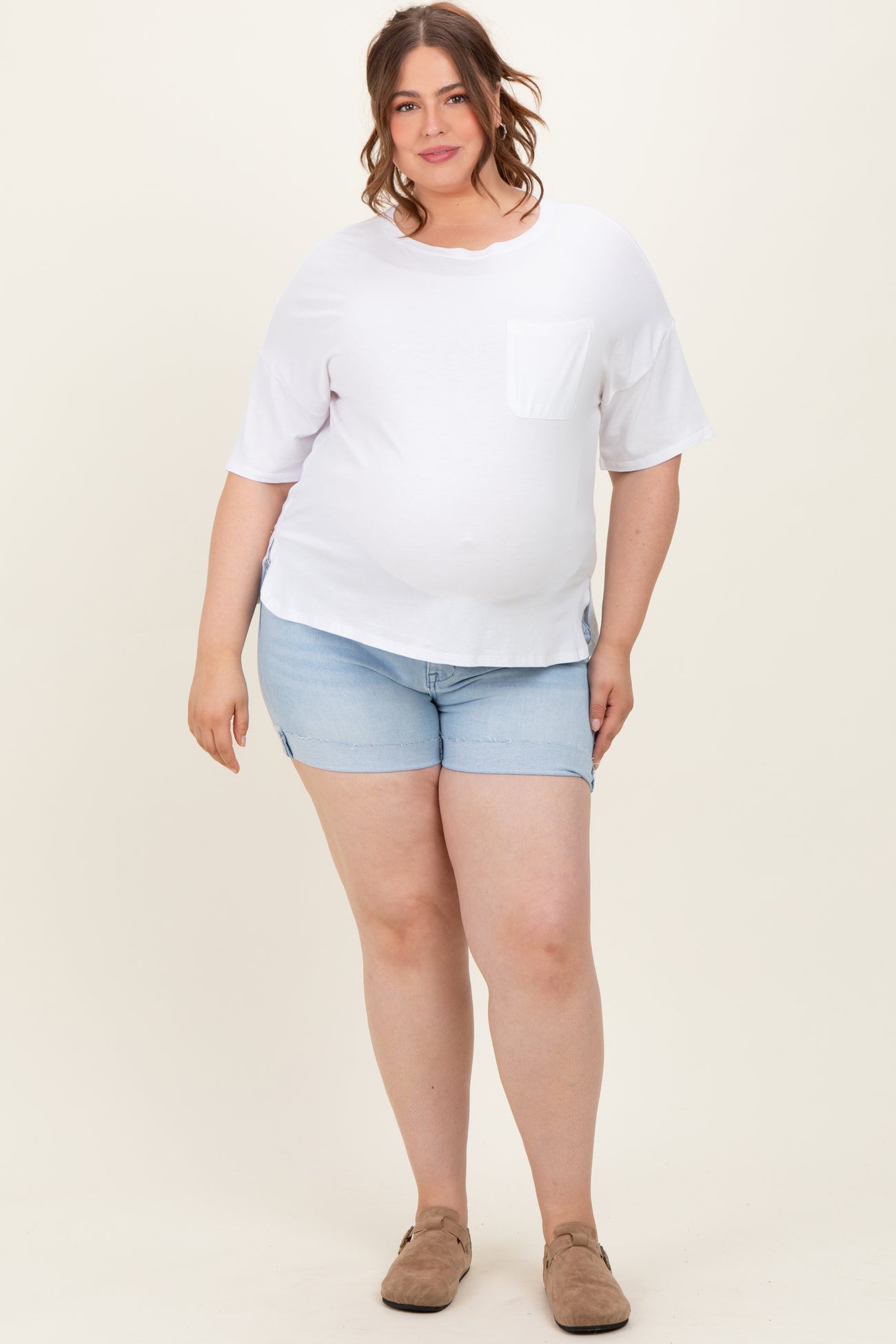 woman wearing a white short sleeve maternity top with a pocket and light blue denim shorts, showing her baby bump