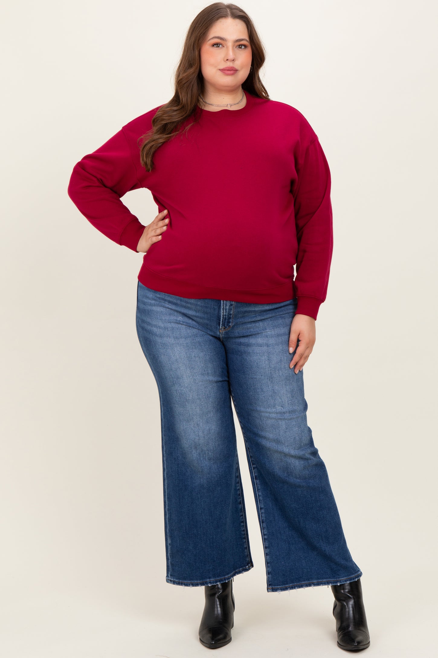 woman wearing a maroon maternity plus sweatshirt and wide-leg jeans, showing her baby bump