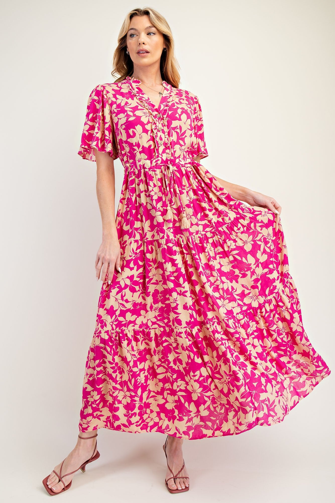 woman wearing a pink floral maxi dress with short sleeves and a tiered skirt, posing gracefully