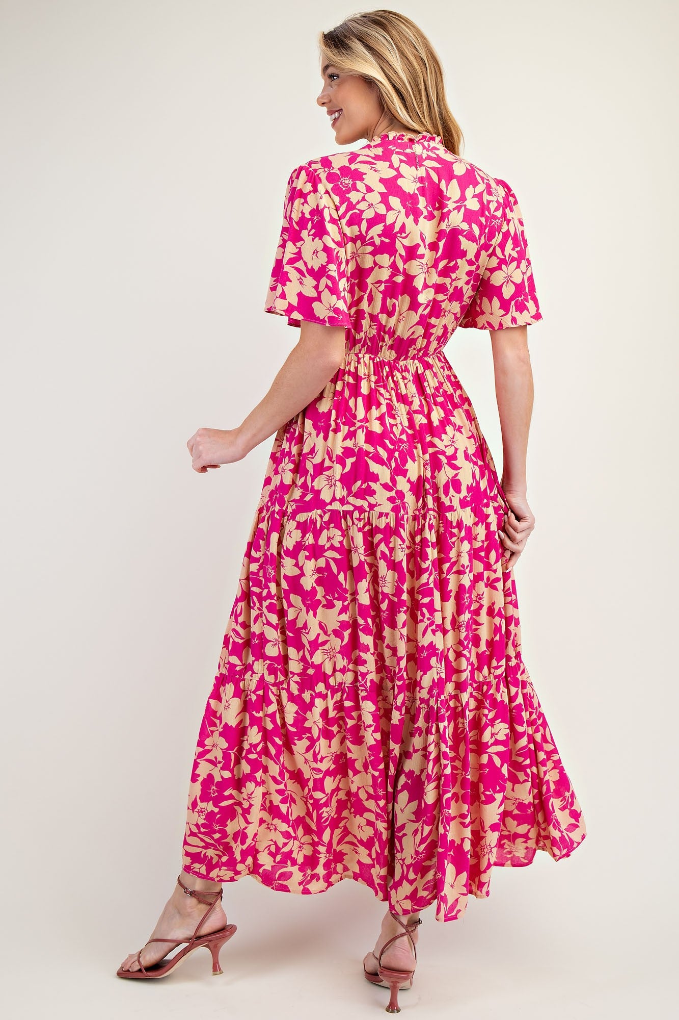 woman wearing a pink floral maxi dress with short sleeves and a tiered skirt, viewed from the back