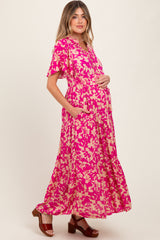 woman wearing a pink floral maternity maxi dress with pockets and short sleeves, showcasing her baby bump