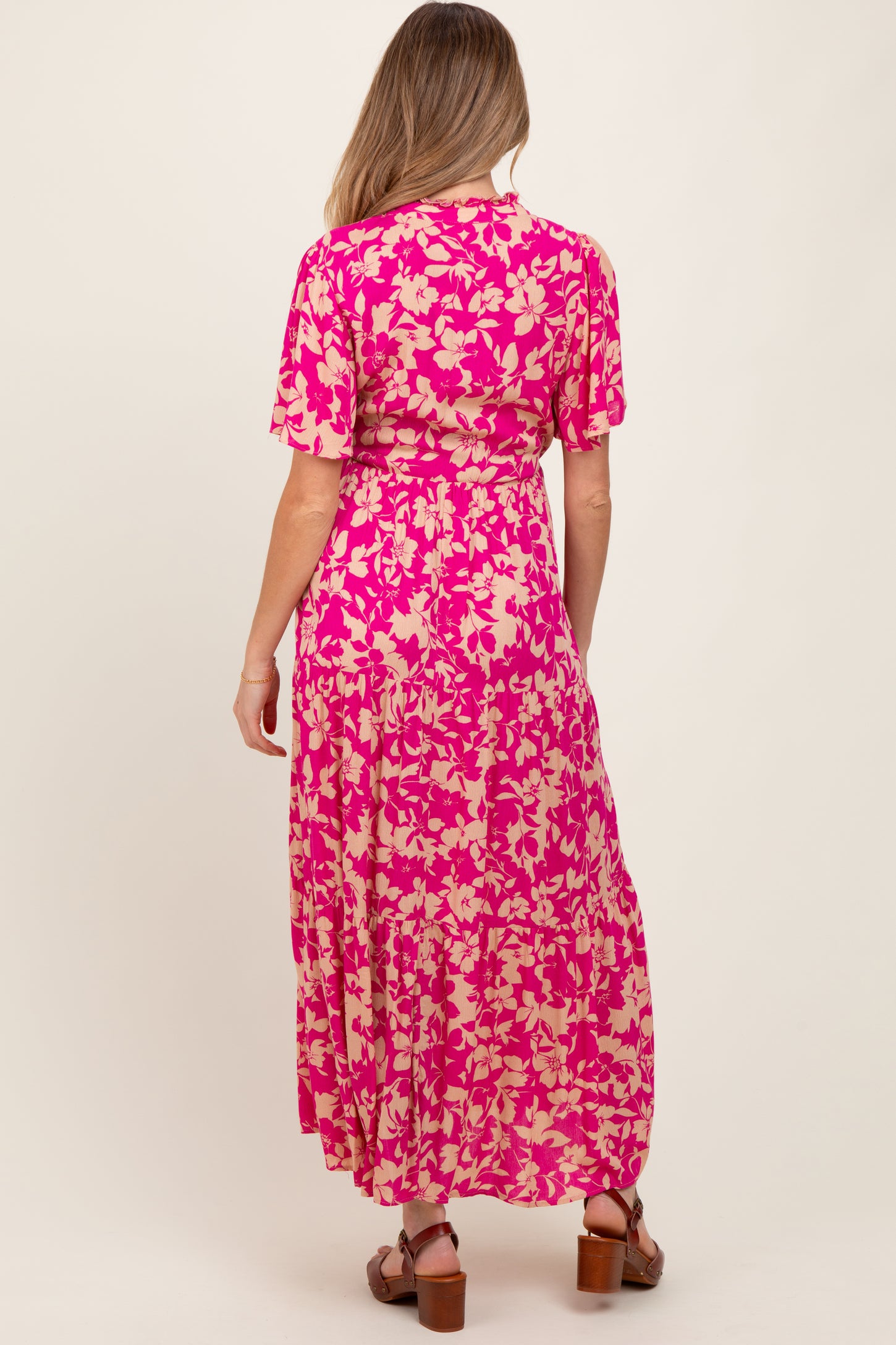 woman wearing a pink floral maxi maternity dress with short sleeves and a flowy silhouette, showing a baby bump
