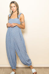 woman wearing a light blue floral print jumpsuit with ruffled straps and loose-fitting legs