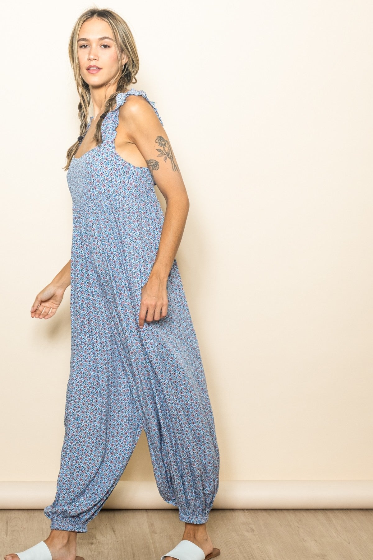 woman wearing a light blue floral jumpsuit with ruffled straps and a relaxed fit, posing sideways