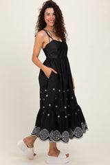 woman wearing a black maxi dress with silver embroidery and pockets, featuring a tiered hem and adjustable straps