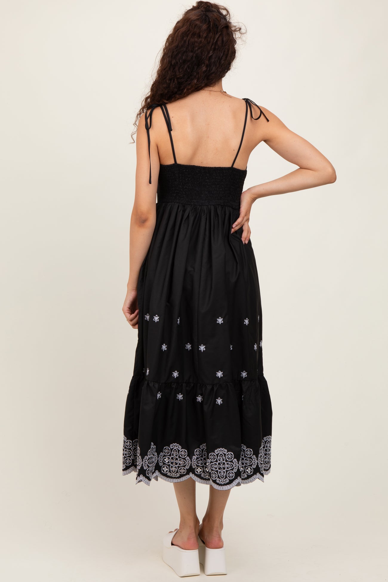 woman wearing a black sleeveless maxi dress with embroidered floral details and a smocked bodice, shown from the back