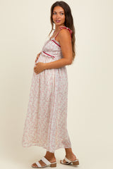 woman wearing a long floral maternity dress with adjustable straps, gently cradling her baby bump