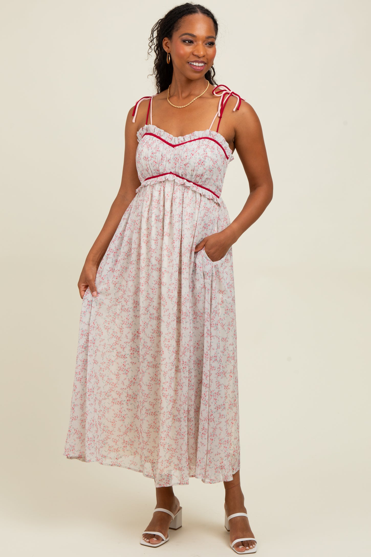 woman wearing a floral maxi dress with tie straps and pockets, featuring a ruffled neckline and red trim