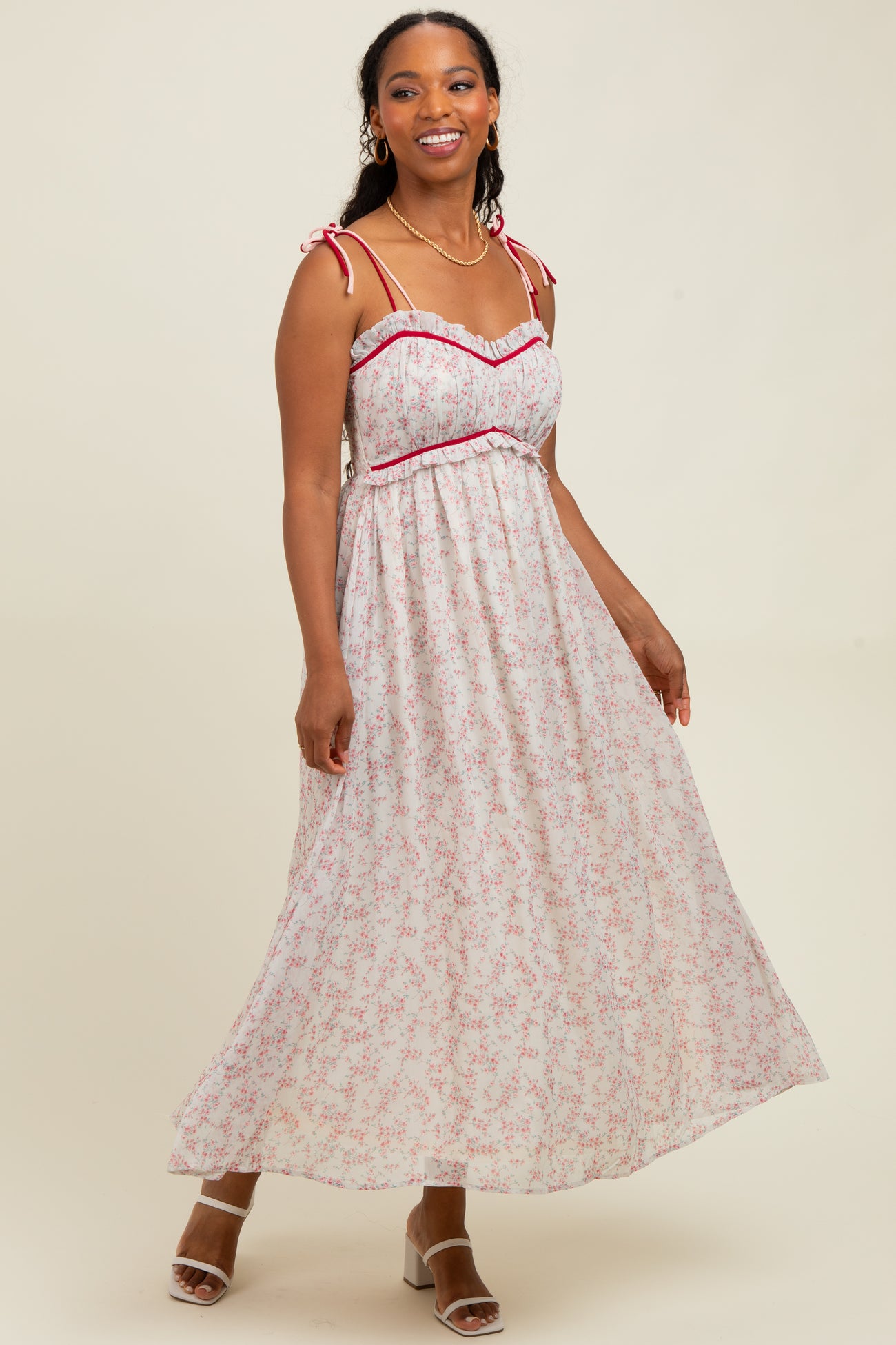 woman wearing a floral maxi dress with red trim and tie straps, smiling against a neutral background