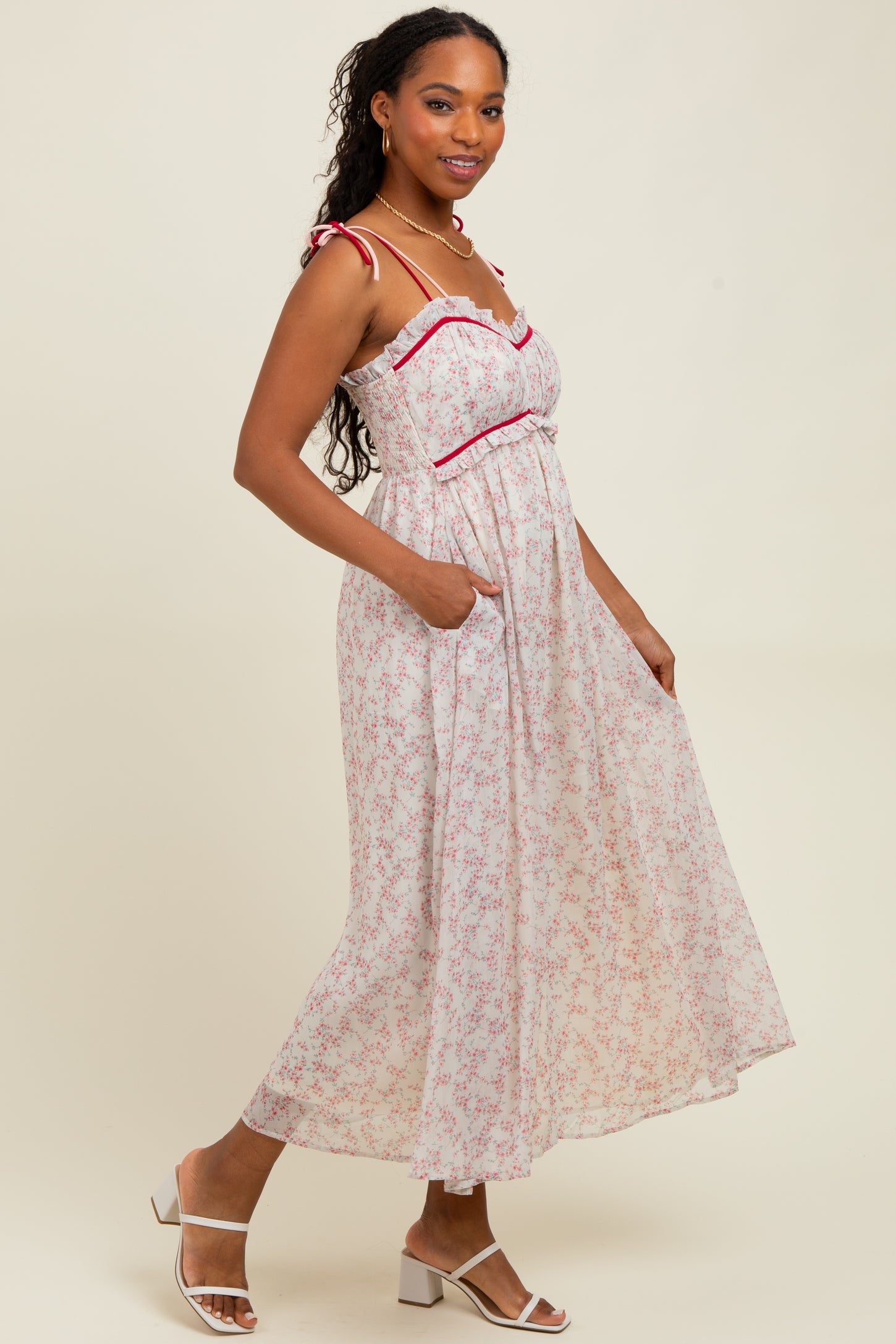 woman wearing a white floral maxi dress with red accents and pockets, standing in a relaxed pose
