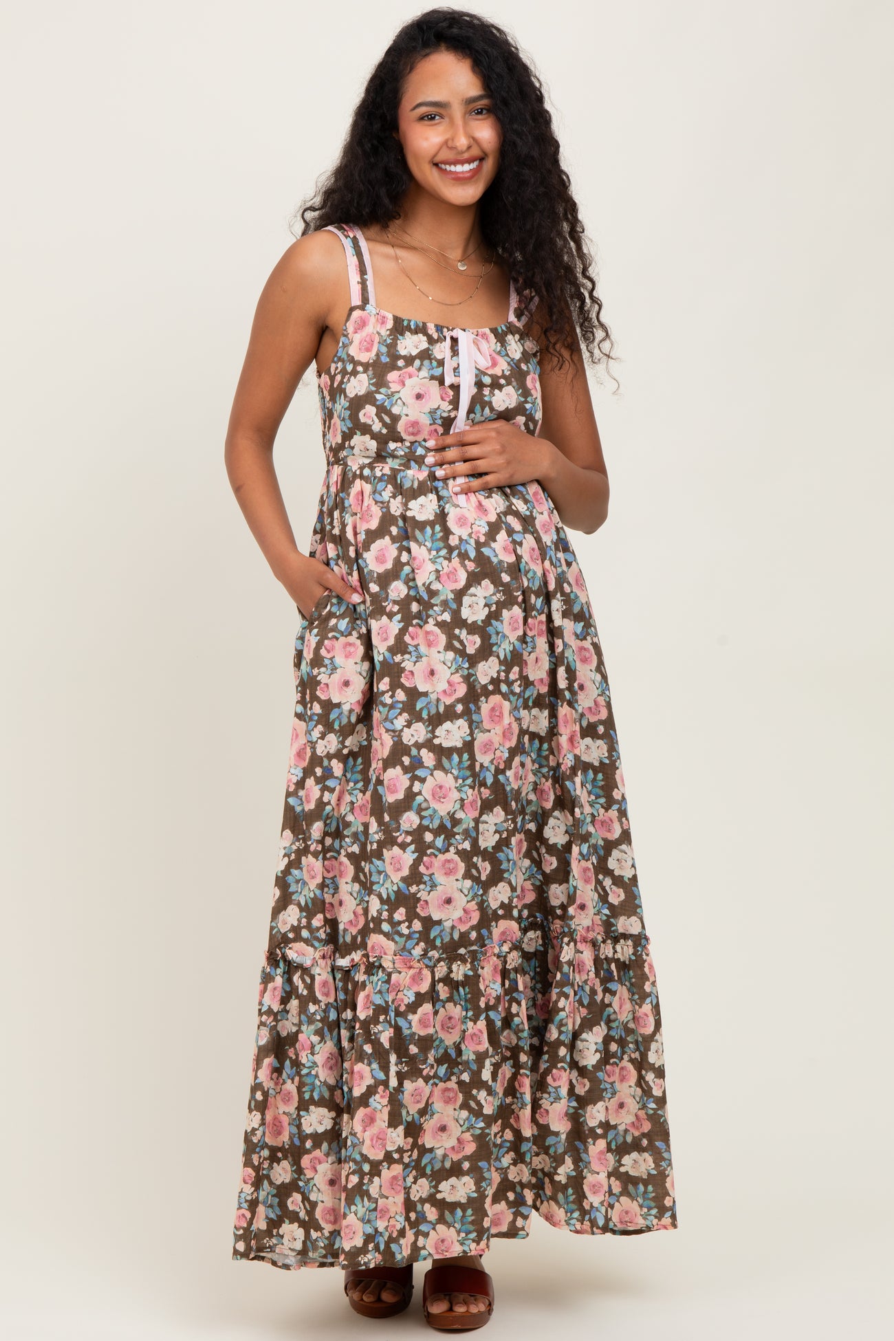 woman wearing a brown floral maternity maxi dress with adjustable straps and a baby bump.
