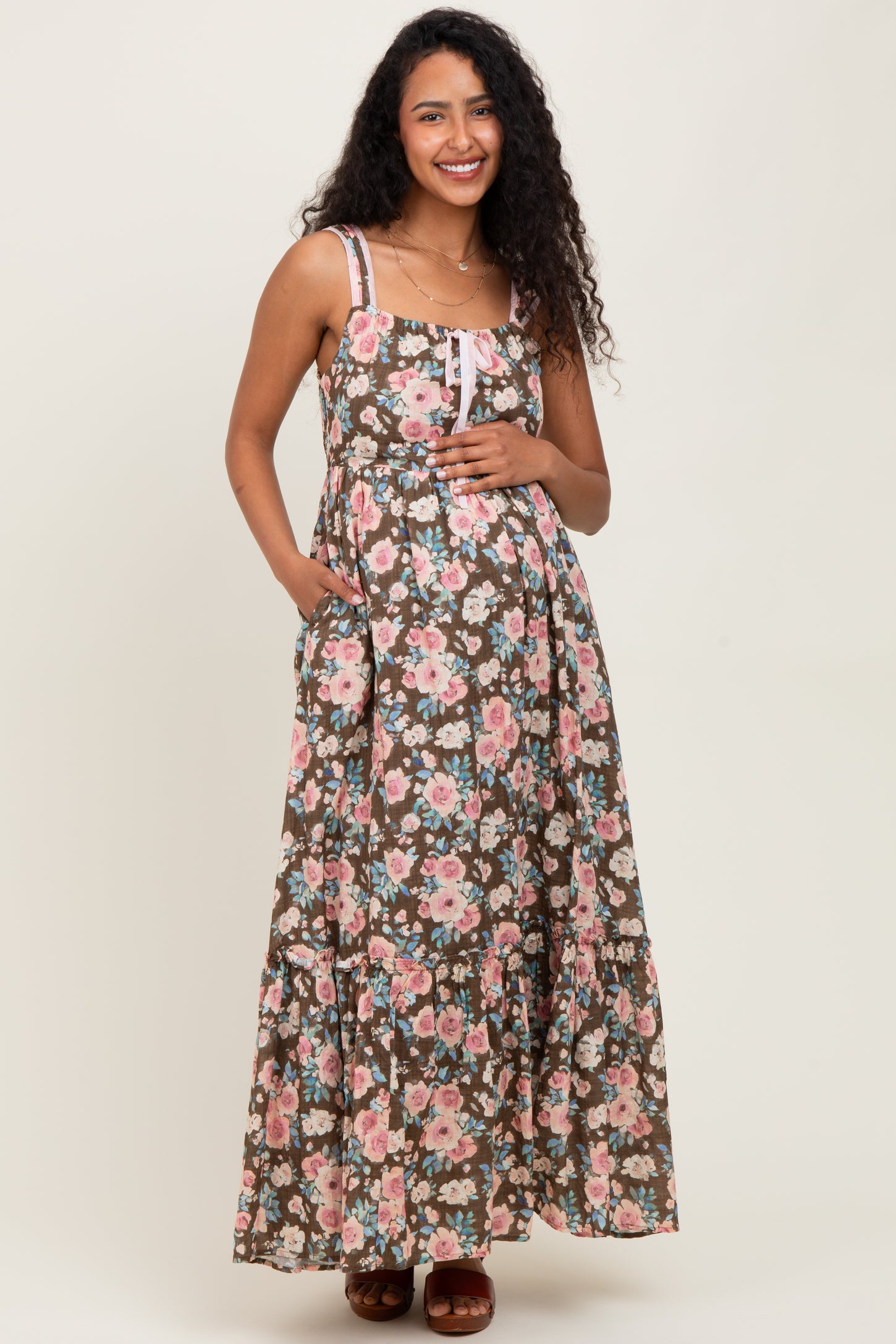 woman wearing a brown floral maternity maxi dress with adjustable straps and a baby bump.