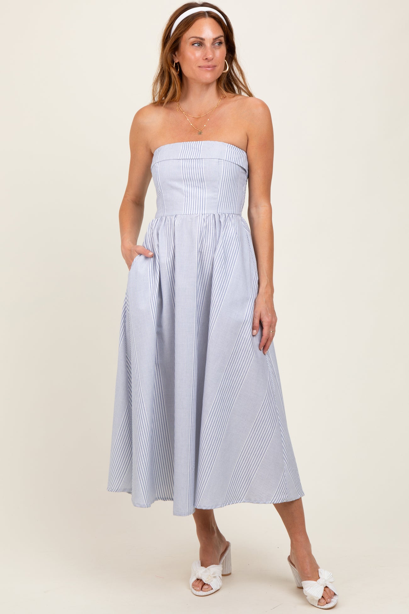 woman wearing a strapless blue and white striped midi dress with pockets and a fitted bodice