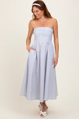 woman wearing a strapless blue and white striped midi dress with pockets, styled with a white headband and white sandals