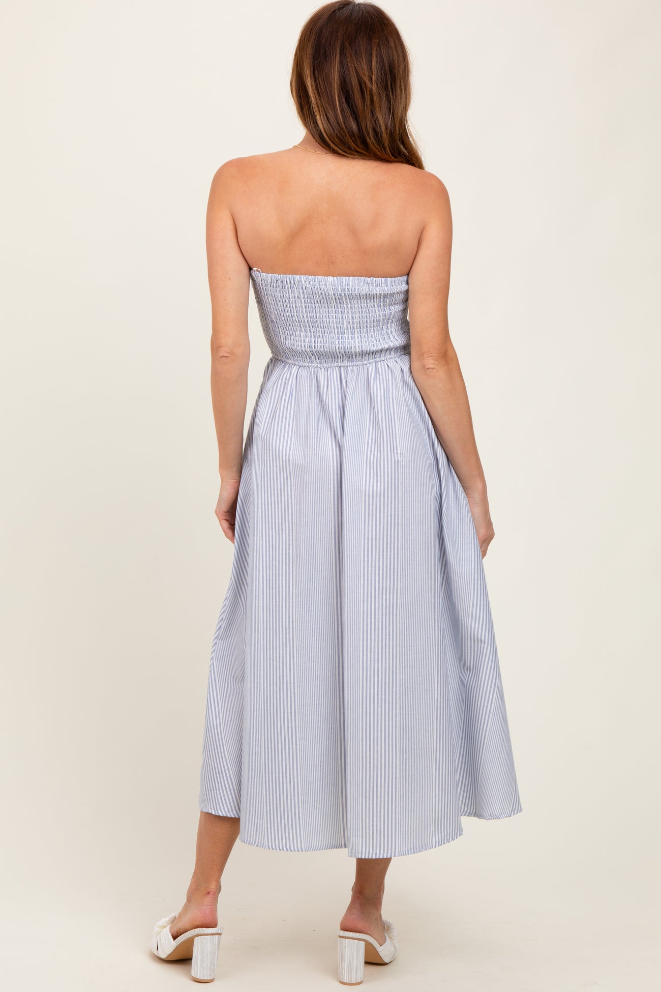 woman wearing a strapless blue and white striped midi dress with a smocked bodice and flowing skirt