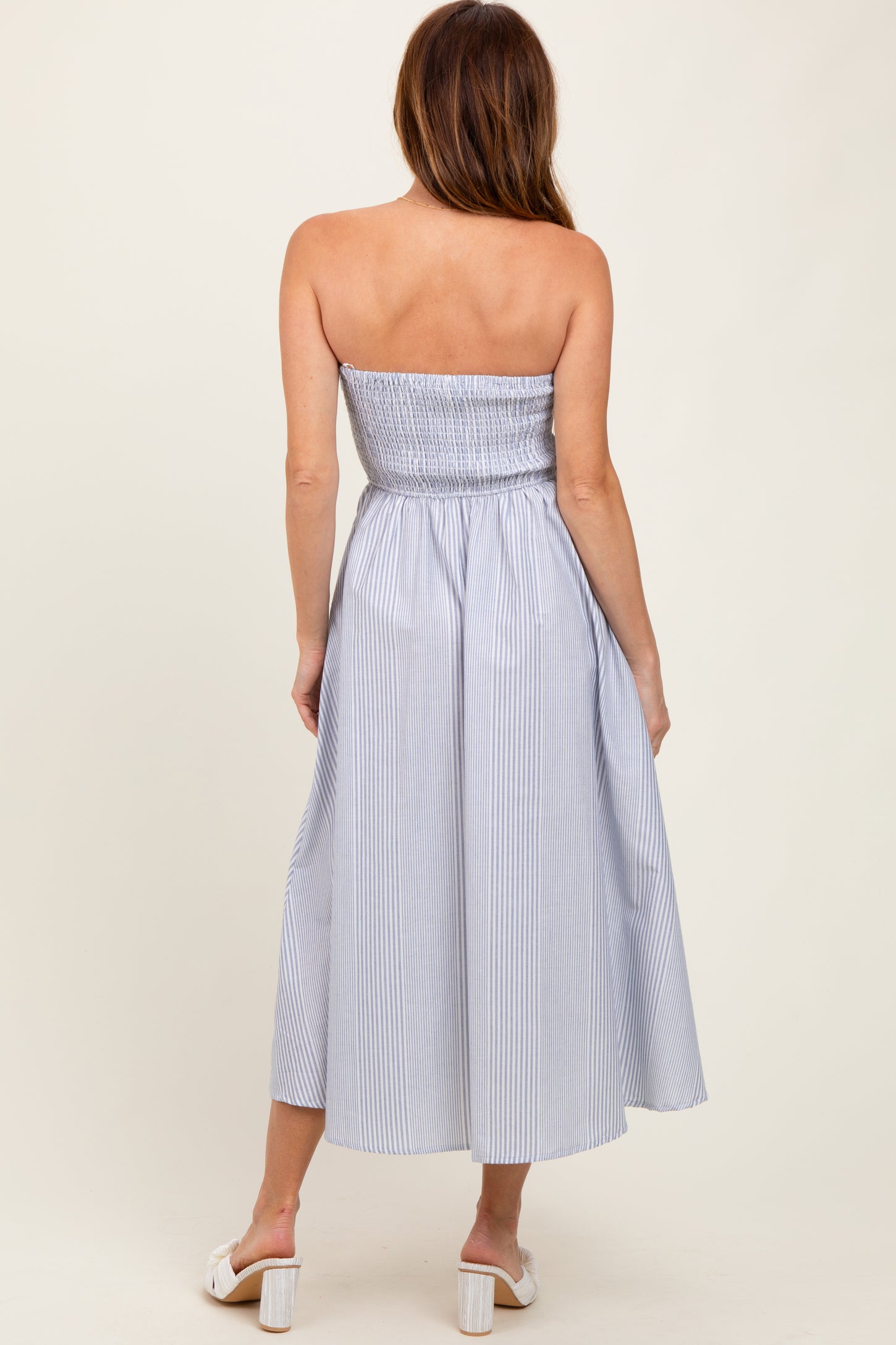 woman wearing a strapless blue and white striped midi dress with a smocked bodice and flowing skirt