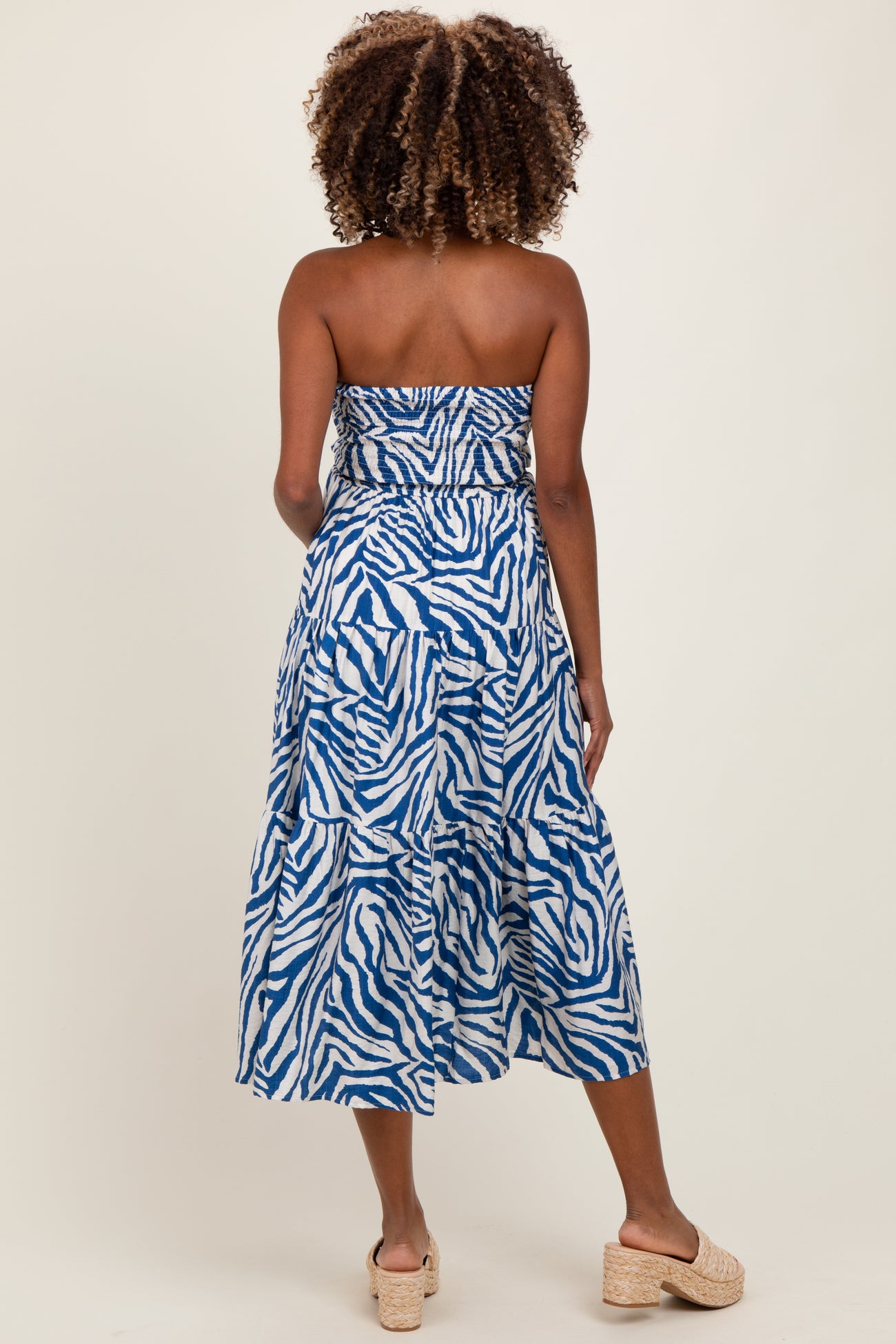 woman wearing a blue and white strapless maternity dress with a tiered skirt, showing her back and styled with sandals