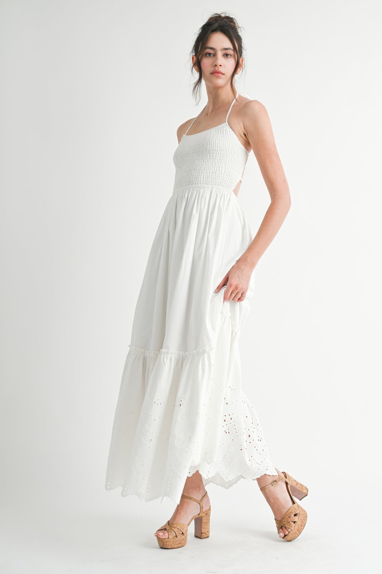 woman wearing a white maxi dress with a smocked bodice and eyelet detailing, paired with brown platform heels