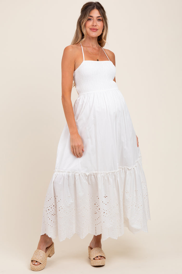 woman wearing a white maternity maxi dress with smocked bodice and eyelet hem, showing her baby bump