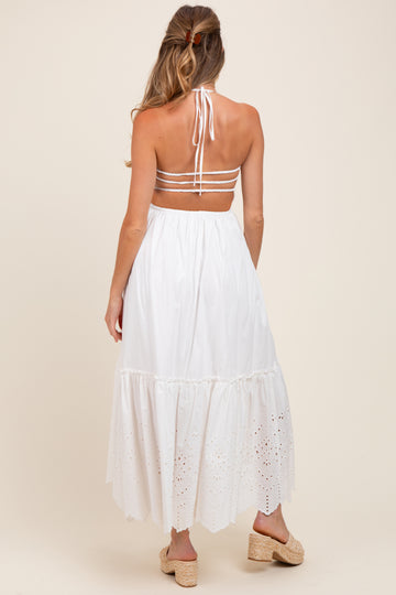 woman wearing a white maternity maxi dress with a halter neckline and eyelet detailing on the lower hem